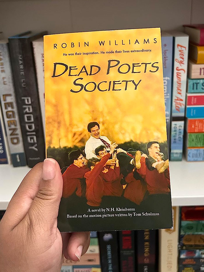 A hand holding "Dead Poets Society" book in front of a bookshelf, highlighting book quotes.