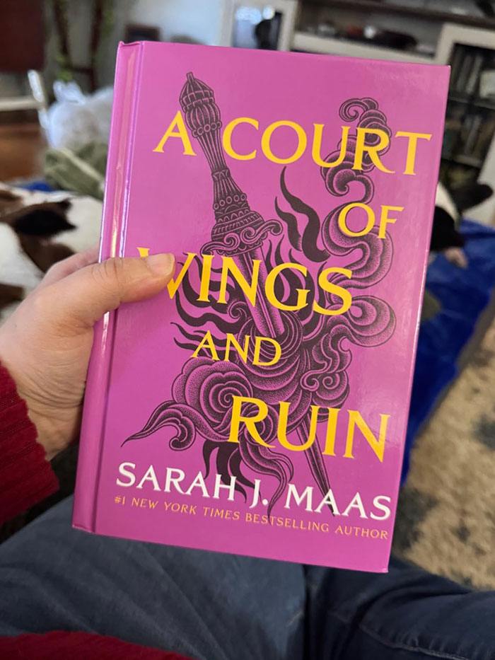 Hand holding "A Court of Wings and Ruin" book with purple cover featuring yellow title.