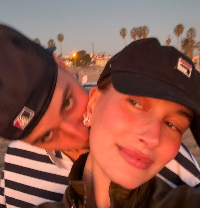 Two individuals in casual attire, wearing caps, enjoy a close moment outdoors at sunset. Two individuals in casual attire, wearing caps, enjoy a close moment outdoors at sunset.