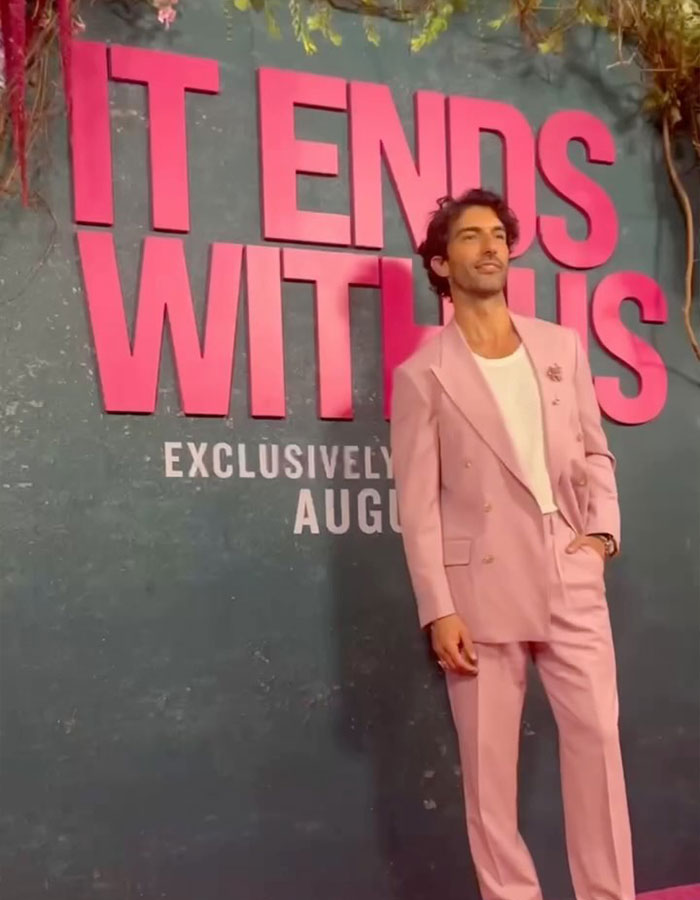 Justin Baldoni in a pink suit at 'It Ends With Us' event, standing confidently by promotional sign. Justin Baldoni in a pink suit at 'It Ends With Us' event, standing confidently by promotional sign.
