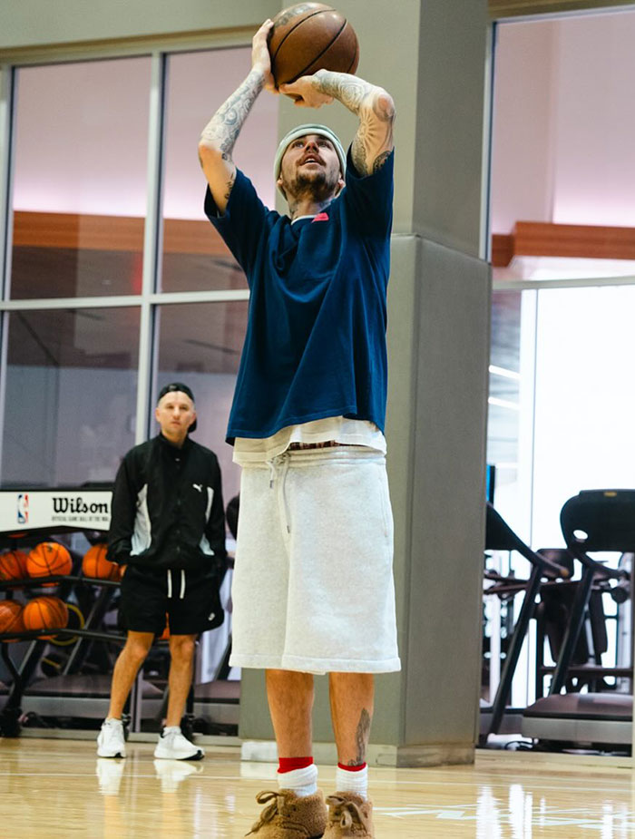 A person in casual wear plays basketball in a gym setting, aiming for a shot. A person in casual wear plays basketball in a gym setting, aiming for a shot.