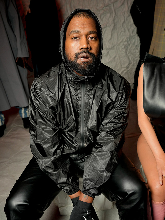 Kanye West in a black outfit sitting indoors. Kanye West in a black outfit sitting indoors.