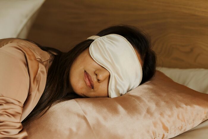A woman wearing a sleep mask, resting peacefully on a satin pillow, illustrating essentials for easier traveling.