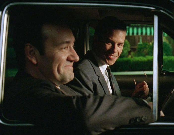 Kevin Spacey and Guy Pearce conversing inside a car, one with a slight smile in L.A. Confidential