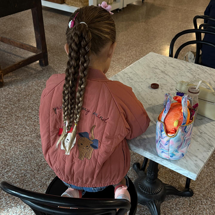 Child with braided hair in a pink jacket sitting at a table.