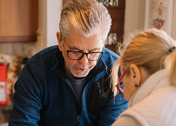 Man in glasses, blue sweater focused on task with woman, related to family and LGBTQ+ topics.
