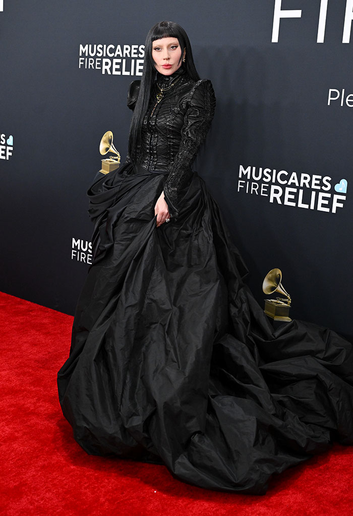 Individual in an elegant black gown on the Grammy Awards red carpet, posing with a golden gramophone trophy.