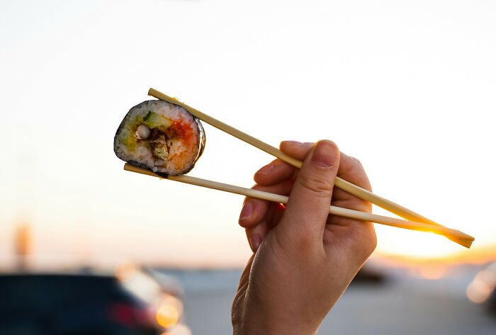 Hand holding sushi with chopsticks at sunset, highlighting multipurpose living.