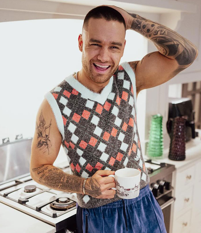 Man in patterned sweater, smiling in kitchen, holding a mug. Celebrities tragically passing.