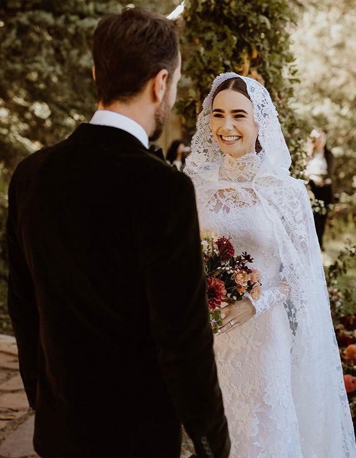 Bride in a lace veil holding flowers, smiling at a groom in a black suit during an outdoor wedding ceremony. Bride in a lace veil holding flowers, smiling at a groom in a black suit during an outdoor wedding ceremony.