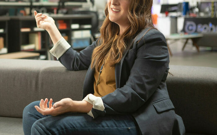 Person sitting on a couch in an office, wearing a dark blazer, related to things wedding guests dislike.