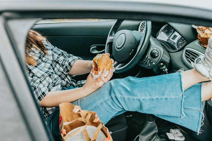 Person eating fast food in a car, symbolizing professions that might become useless soon.