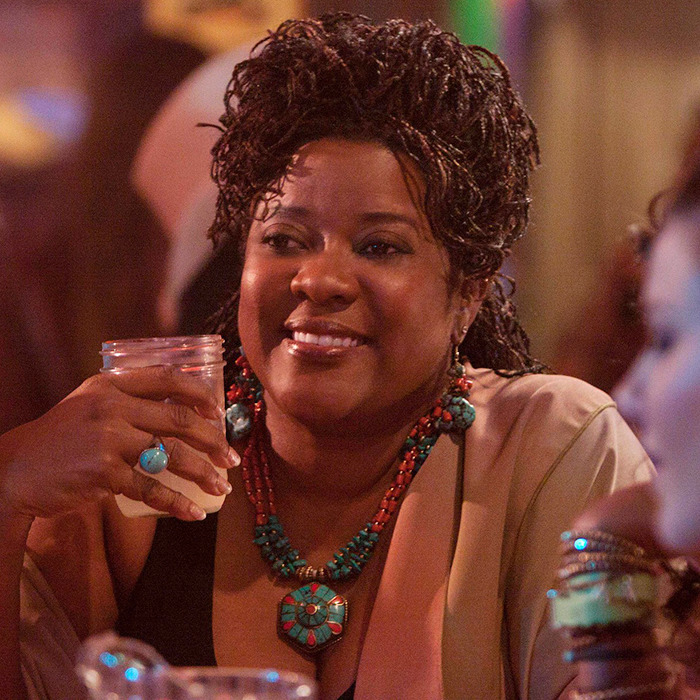 Loretta Devine smiling, holding a drink, adorned with turquoise jewelry, in a dimly lit setting in a scene from "The Client List.