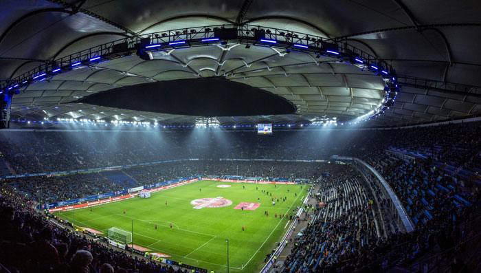 Wide-angle view of a brightly lit football stadium filled with spectators during an evening match.