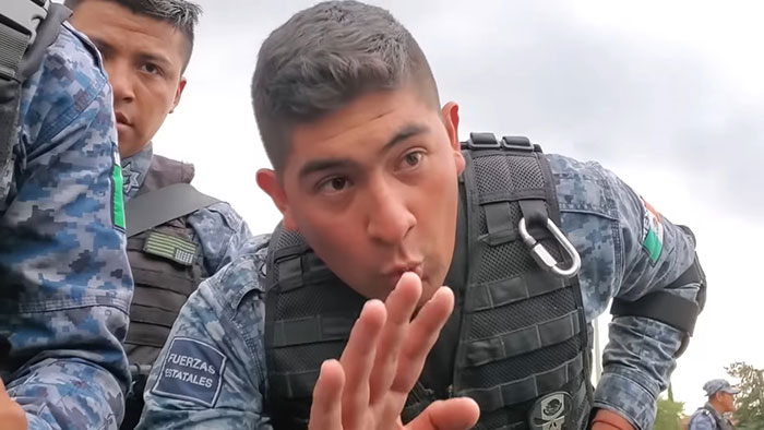 Hombre prepotente vestido de uniforme táctico gesticulando frente a la cámara al aire libre.