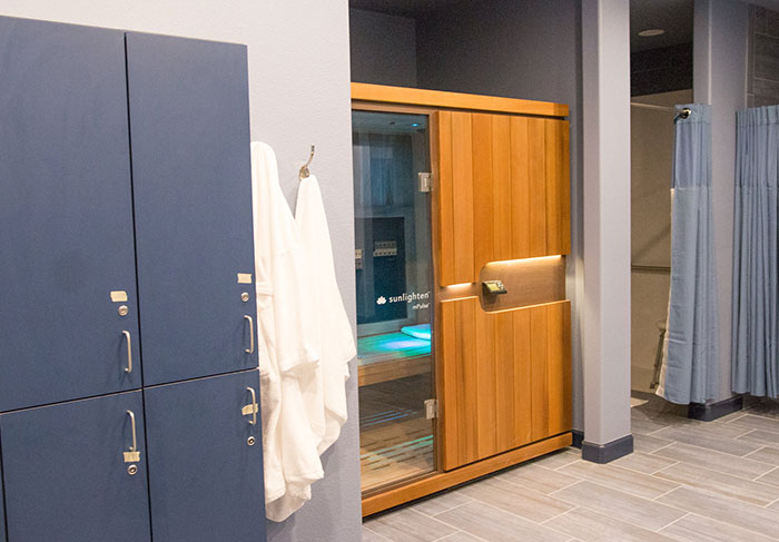 Women&rsquo;s changing room with lockers, robes, and a sauna, featuring blue and wood accents.