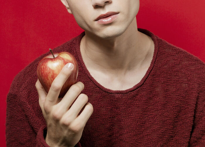 Person holding an apple against a red background, illustrating rare cosmetic procedures.
