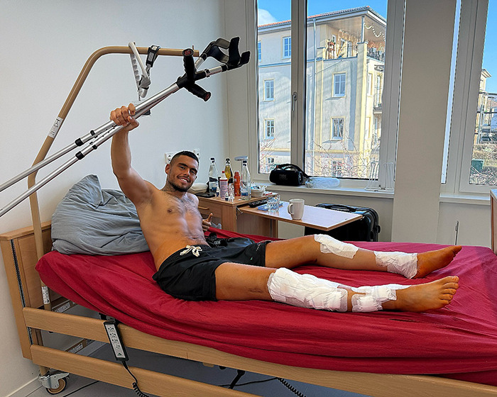 Leon Otremba in hospital bed with crutches, bandaged legs, smiling, and showcasing his recovery experience. Leon Otremba in hospital bed with crutches, bandaged legs, smiling, and showcasing his recovery experience.