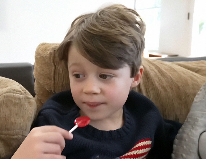 Young boy with a lollipop sitting on a couch. Autism breakthrough helps nonverbal child speak.