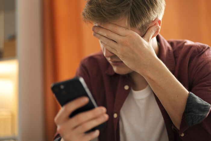 Person in a maroon shirt holding a phone, covering their face, conveying emotional reaction, symbolizing love and care.