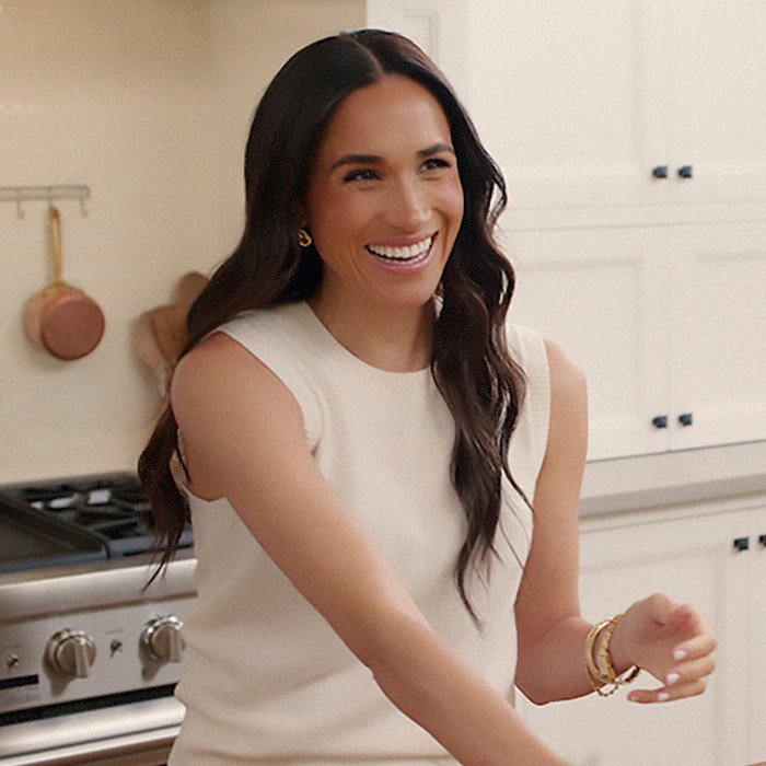 Meghan Markle in a kitchen, wearing a sleeveless top and bracelets.