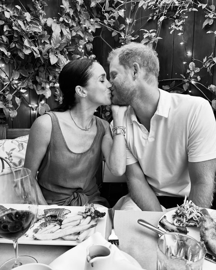 A couple kissing at a dining table surrounded by plants, enjoying a meal together.