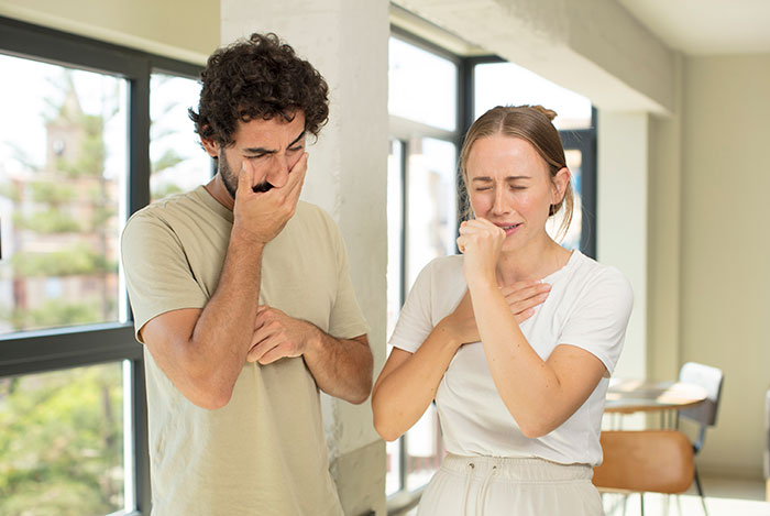 A man and woman laughing in a bright room, covering their mouths with their hands, depicting humor and human interaction.