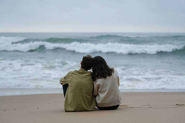 A couple sitting on a beach, embracing and watching the waves; related to lies men tell partners.