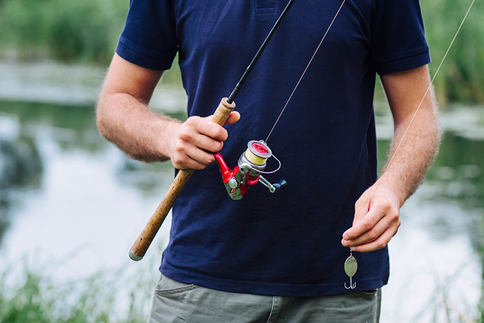 Man holding fishing rod by a lake, showcasing outdoor leisure activities.