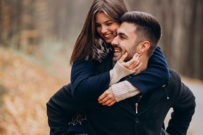 A couple laughing in an autumn forest, highlighting relationship dynamics and honesty amidst fallen leaves.