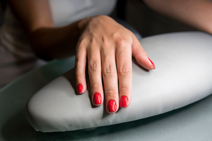 A hand with red nail polish rests on a cushion.