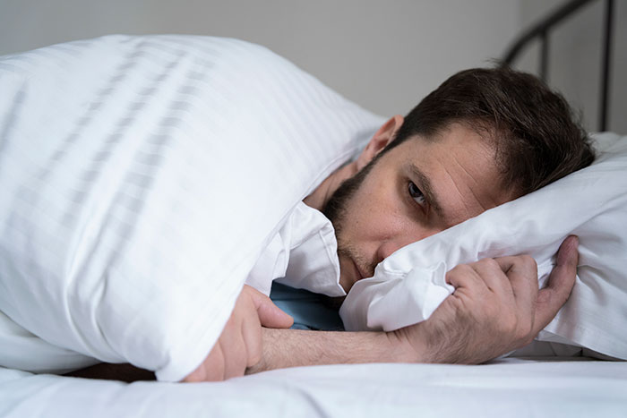 Man lying in bed with his head on a pillow, appearing thoughtful, related to lies men tell their partners.