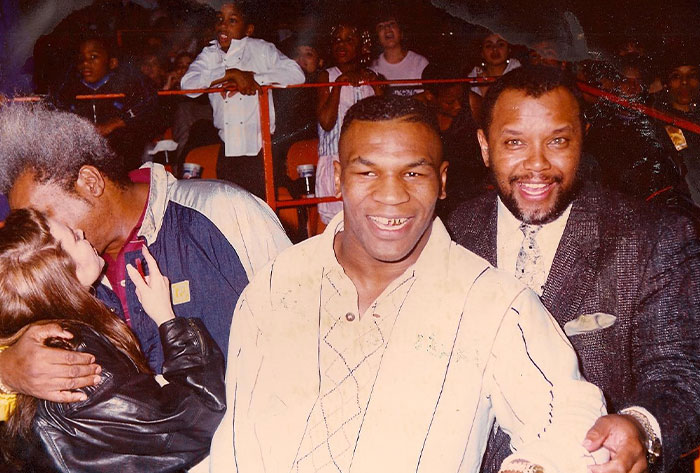Mike Tyson smiling, wearing a beige shirt, with friends in a lively crowd, highlighting his net worth recovery journey.