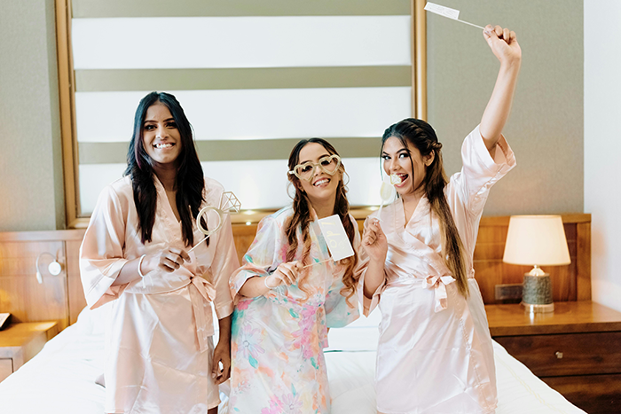 Three women in robes, smiling and holding party props, celebrating in a bedroom setting. Three women in robes, smiling and holding party props, celebrating in a bedroom setting.