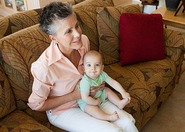 Grandmother with grandson on a patterned sofa, both smiling, showcasing family dynamics and relationships.