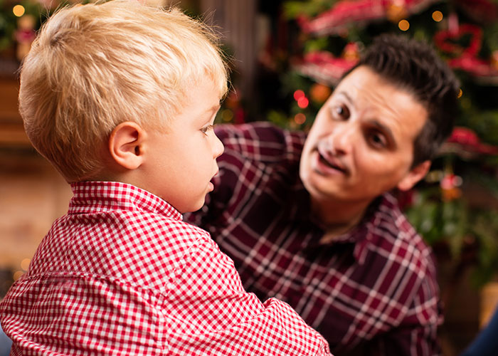 Man speaking to a young boy in plaid shirts, near a decorated Christmas tree, illustrating family conflict over renaming.