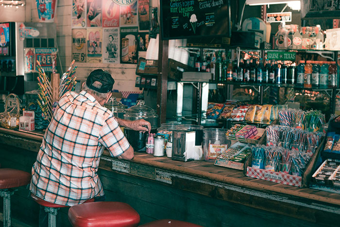 Older man sitting at a vintage store counter surrounded by nostalgic items, reflecting on life regrets.