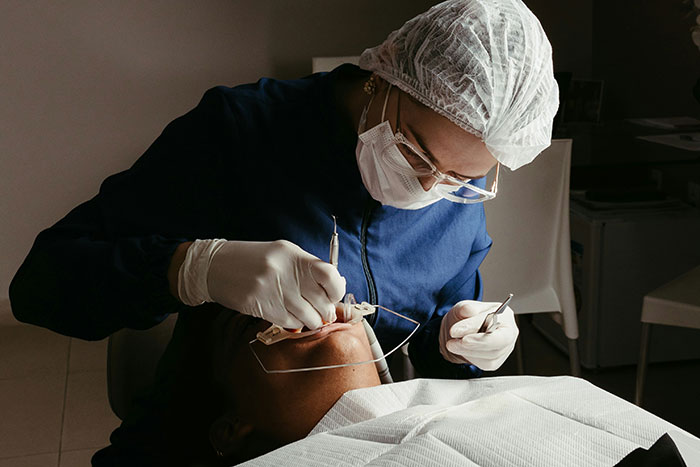 Dentist in blue scrubs and cap working on a patient, possibly reflecting a common life regret related to dental care.