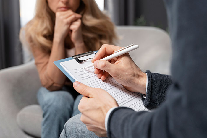 Person reflecting on life regrets during a counseling session, holding a clipboard and pen, contemplating decisions.