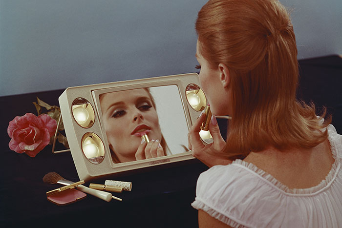 A woman applying lipstick in front of a vintage mirror, reflecting on life regrets.