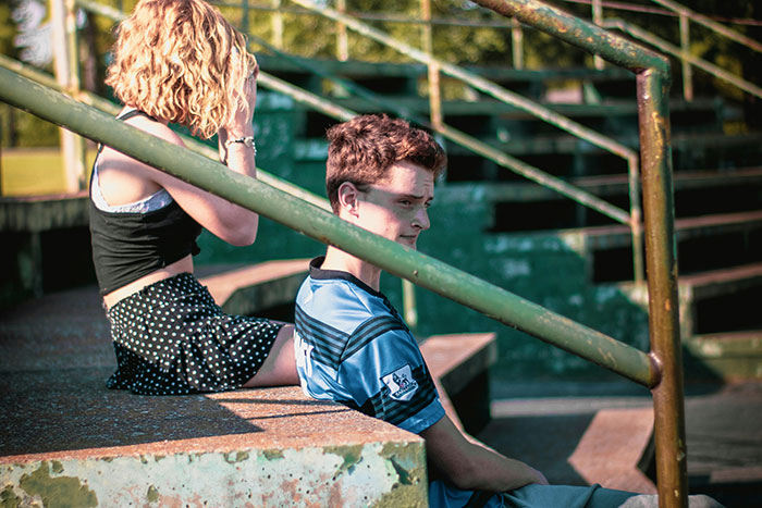 Two people sitting on outdoor stairs, reflecting on life regrets amid a sunny, green setting.