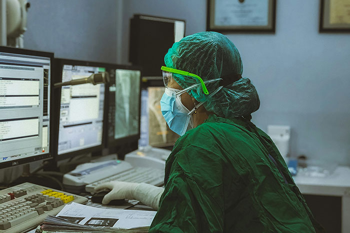 Medical professional in scrubs and mask working at a computer, representing life regrets in healthcare decisions.