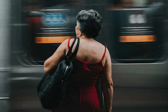 Older woman in a red dress standing near a moving train, reflecting on life regrets.
