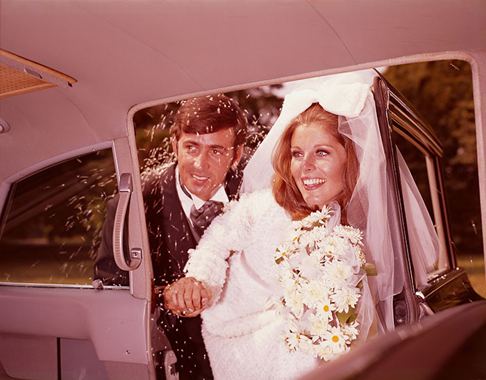 Bride and groom entering a car, possibly reflecting on life's biggest regrets, surrounded by well-wishers.
