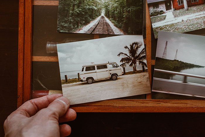 A hand holding a photo of a van parked by palm trees, evoking life regrets and nostalgia.