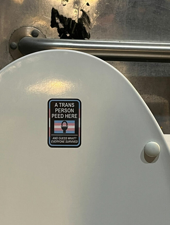 Sticker on a toilet saying "A trans person peed here. Everyone survived," illustrating peak internet humor.
