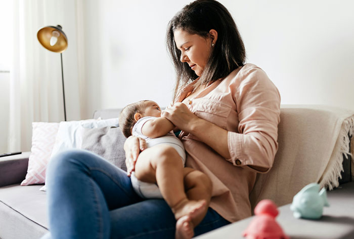 Mom holding baby on sofa, showing concern over 14YO helping responsibilities. Mom holding baby on sofa, showing concern over 14YO helping responsibilities.