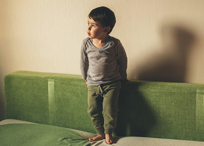 Young boy in a thoughtful pose on a green couch, highlighting family dynamics and strict parenting decisions.