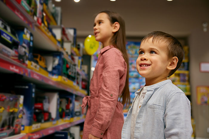 Kids in a store looking at toys on shelves, with a boy smiling and a girl observing in a pink dress. Kids in a store looking at toys on shelves, with a boy smiling and a girl observing in a pink dress.