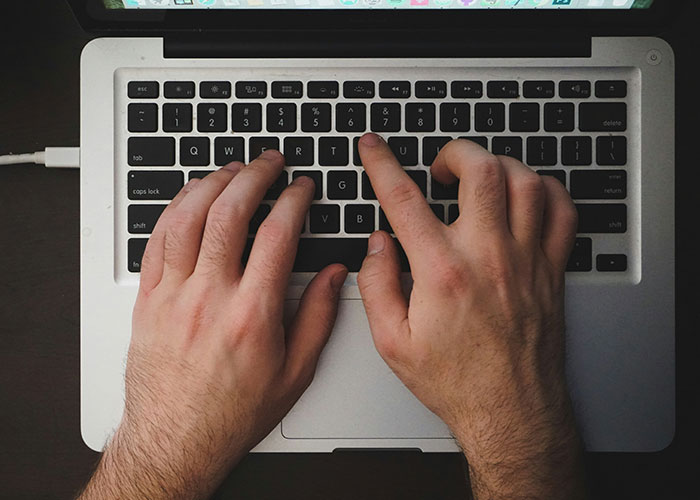 Hands typing on a laptop keyboard, capturing public conversation details.